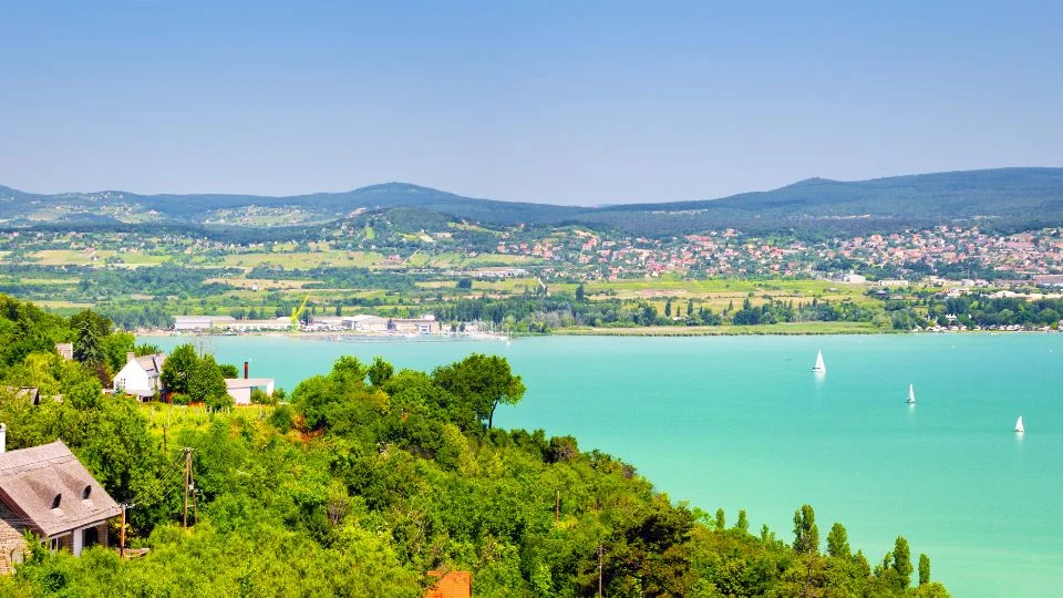 A Balaton gyönyörű panorámája, zöld dombokkal és vitorlásokkal.