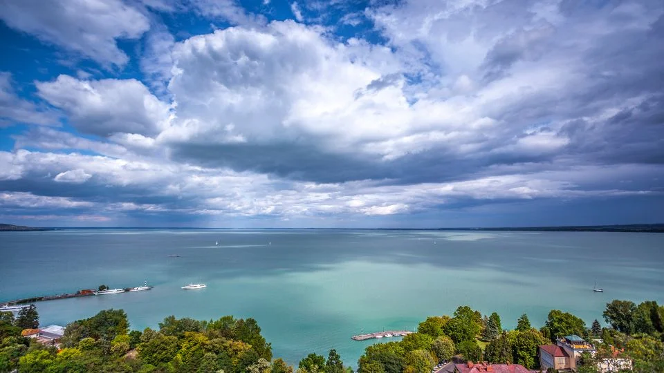 A Balaton gyönyörű panorámája, felhős égbolttal és nyugodt vízfelülettel.