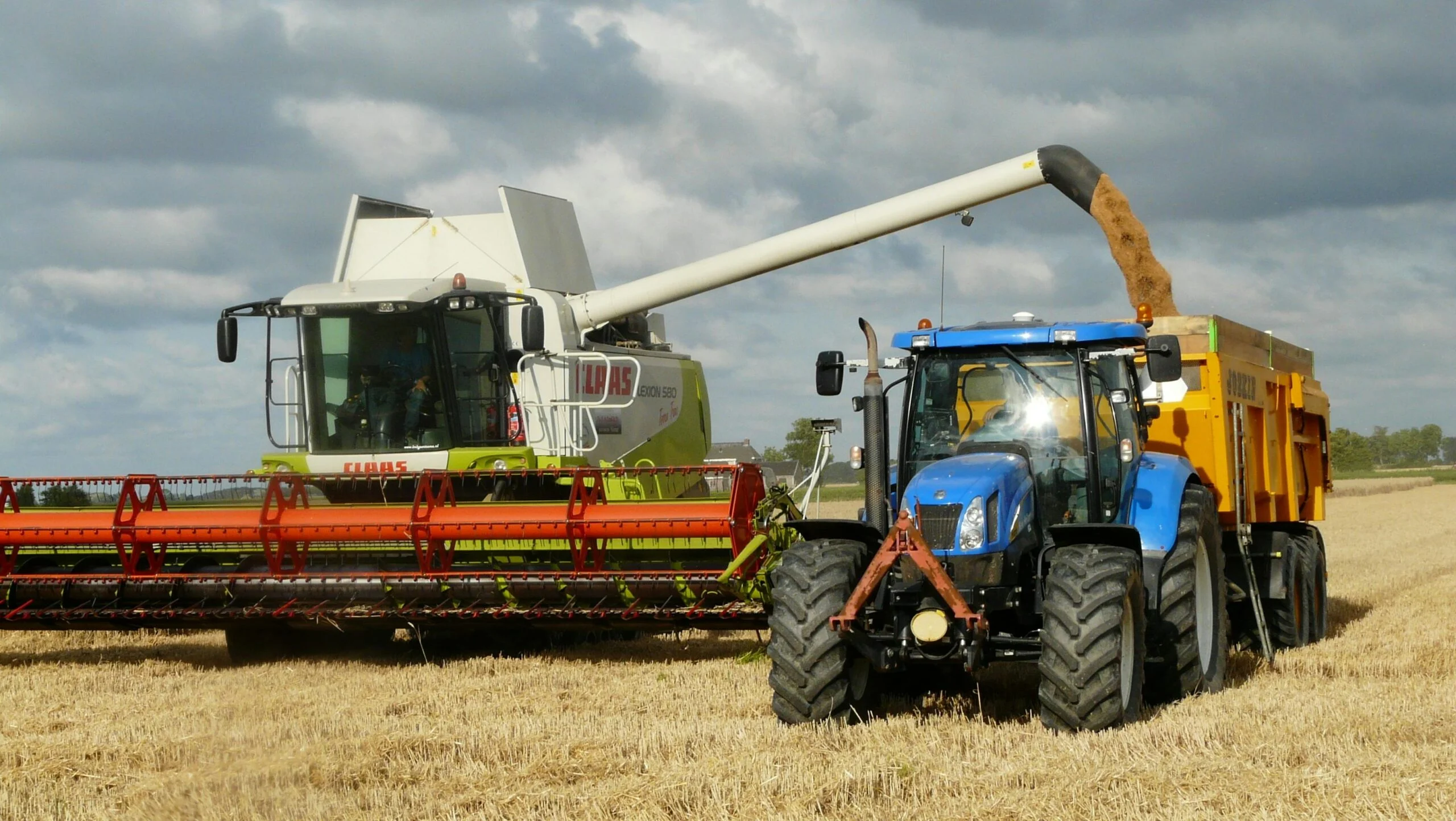 Egy kombájn és egy traktor dolgozik a mezőn, aratás közben.
