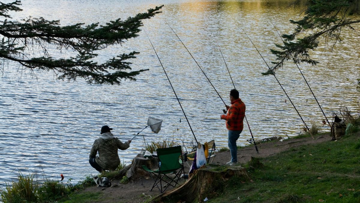 Két horgász ül a vízparton, egyikük hálót használ, míg a másik a botját tartja.